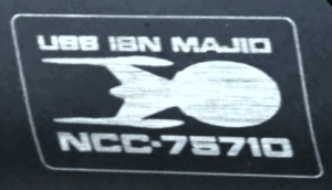 Emblema della USS ibn Mājid NCC-75710 visto sulla valigetta di Cristóbal Rios in Broken Pieces.